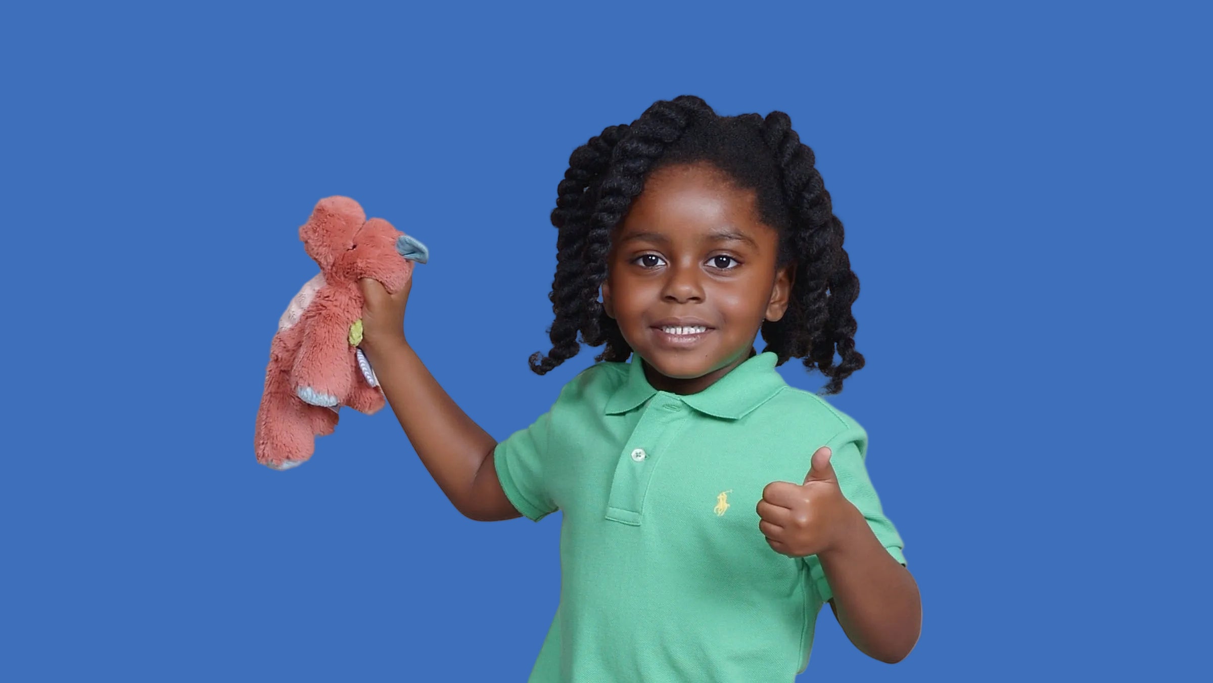 Child wearing a green polo shirt and blue shorts, holding a pink toy and giving a thumbs-up.
